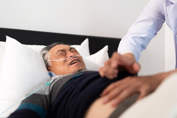 scene of bedridden patient, elderly hopeless senior man lying on bed with oxygen mask by doctor. home caregiver nurse visit retirement patient for health check up recovery process medical service