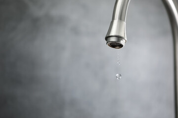 Water saving concept. Water dripping from tap against grey background, closeup. Space for text