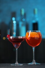 Glasses of tasty cocktails on dark table against blurred background, bokeh effect