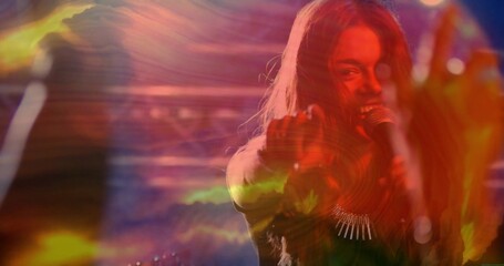 Performing singer in dark gear pointing to viewer on stage, with mic, necklace, lights, copy space