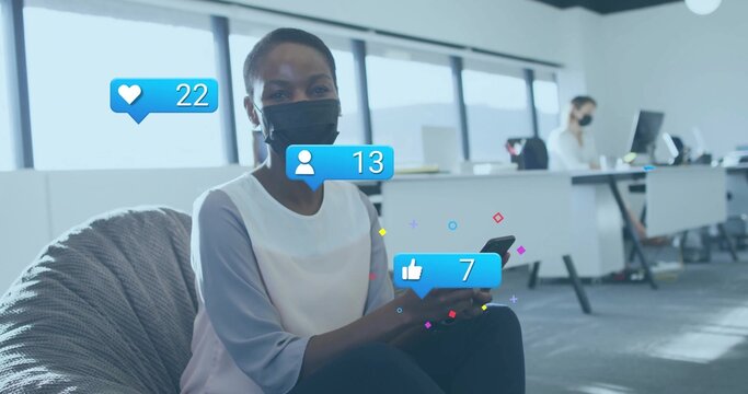 Holding smartphone masked office worker scrolling feed in lounge area with overlay icons