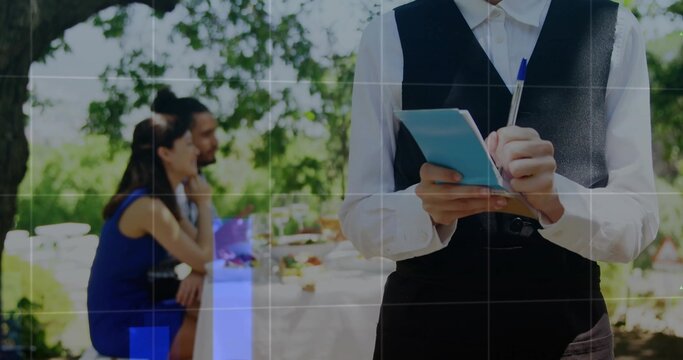 Taking order male server wearing black vest at al fresco terrace, with blue notepad, copy space