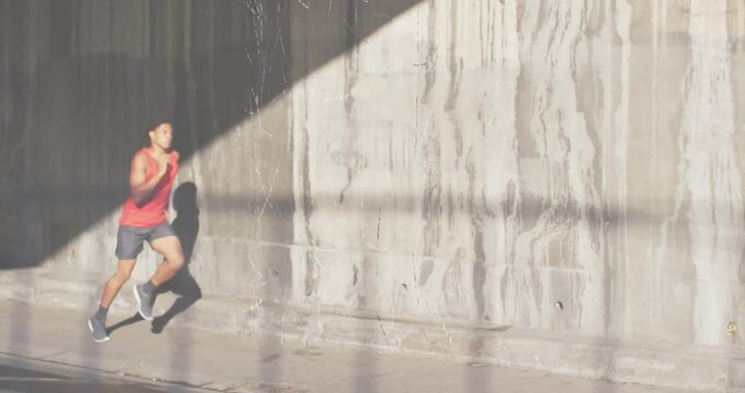 Male runner entering underpass with grid shadows and crossing sunlit triangle for fitness training