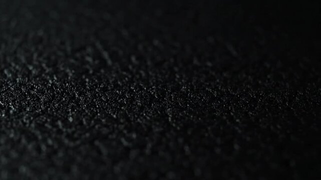 Selective focus on a rough, black, granular surface creating an abstract textured background.