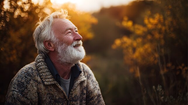 Portrait of happy senior man with white beard looking up in autumn nature background