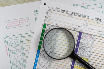 確定申告書と青色申告決算書と虫眼鏡で税務調査のイメージ