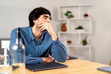 Naklejka premium Young man suffering depression, drinking alcohol at home