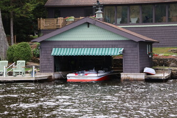 A large wooden boathouse on a lake with a red boat moored inside.