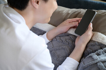The hand of a Japanese man operating a smartphone in bed