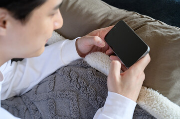 ベッドでスマホを操作する日本人男性の手元