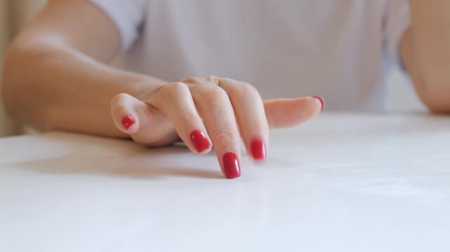 A woman with beautiful red nails taps her finger on the table