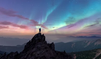 Fototapete Nordlichter Person Standing On Rocky Peak Under Aurora Borealis Over Mountain Range at Dusk  © edb3_16