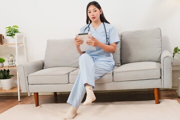 Young healthcare professional in scrubs sitting on couch, holding tablet, ready for consultation or telehealth session