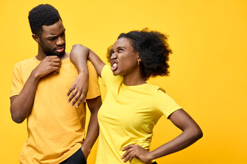 Obraz premium African American couple expressing playful disagreement in matching yellow shirts against a vibrant yellow background, showcasing emotions of frustration and humor