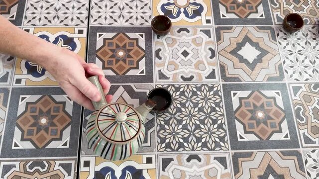 Pouring Tea Into Cup on Patterned Tile Tabletop