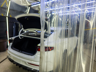 Car parked indoors in a garage with open trunk. Industrial setting emphasizes functionality, showcasing tools and detailing equipment in bright daylight.