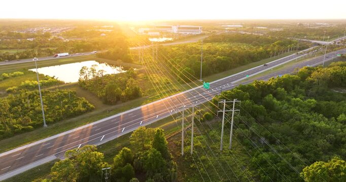 High voltage power lines on steel tower span across busy Florida highway with cars in motion. Electrical energy transmission over transportation route