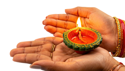 Two hands cradling a lit diya, a small oil lamp, on a black backdrop