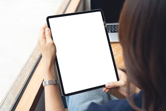 Mockup blank screen digital tablet. Woman holding digital tablet with blank white screen with laptop computer on table at coffee shop, template for web app design or social media marketing