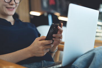 Happy young asian woman using mobile phone and laptop computer remote working at coffee shop. Woman using smartphone for online shopping and internet banking via mobile app, social media networking