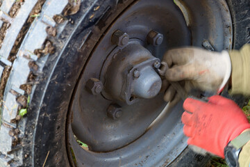 ​A close-up view shows the process of repairing a wheel of agricultural machinery, likely a mini-tractor, with hands in multi-colored gloves working on the hub fasteners.