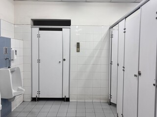 A simple, clean image of a public restroom showing a row of white stalls with metal hardware, a...