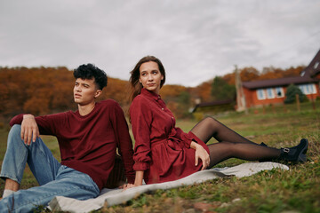 Young couple sits on a blanket in a rural autumn field, sharing a genuine relaxed pose and eye...