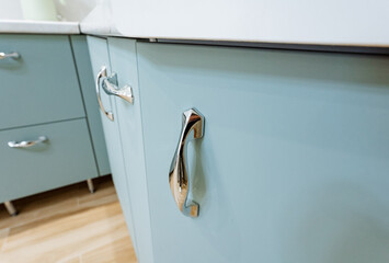 This image features a closeup of a sleek kitchen cabinet with modern pull handles and a soft blue...