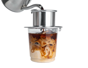 Dark coffee is being brewed through a metal filter into a clear cup with milk