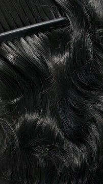 Vertical black hair texture, slow motion of female hand combing long curly hair