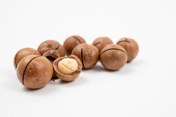 Group of whole and cracked macadamia nuts on white background, with exposed kernels inside broken shells.