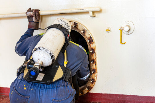 Crew member enters a narrow hatch to provide first aid during a man evacuation drill from a confined space on a merchant ship. - Powered by Adobe