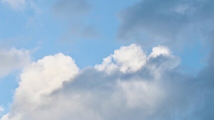 A mix of dark grey storm clouds and bright white cumulus formations against a pale blue sky, showing the transition of weather and dramatic atmospheric contrast.