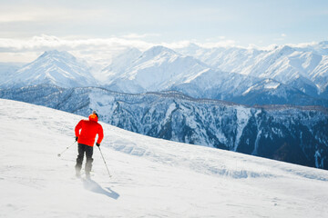 Male adult skier in red jacket go freestyle off piste carving turns to fresh powder mountainside in snowy mountain resort during sunny winter day adventure in alpine high mountains