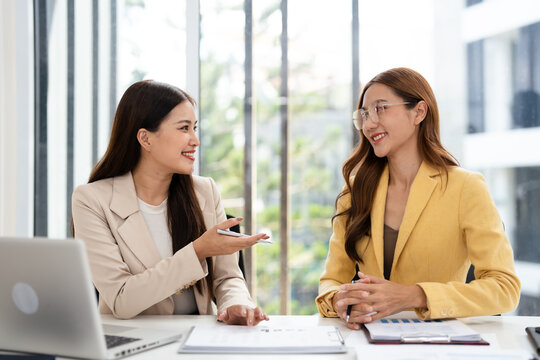Young businesswomen sit at desk in office work together on laptop discuss ideas. female employees colleagues brainstorm on computer at meeting. Teamwork concept.