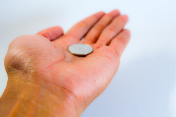 A hand holding a silver coin over white background, concept of money, savings, or economy.