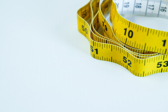 Yellow measuring tape rolled on white background, close-up tool for tailoring and measurement.