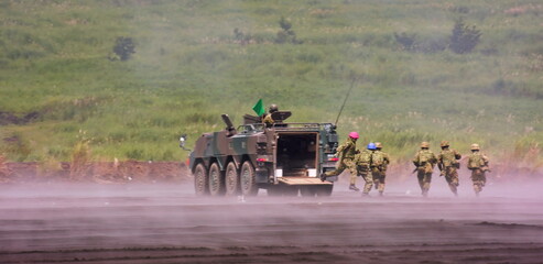 Soldiers in tactical gear disembark from a camouflaged armored transport, running low across a...