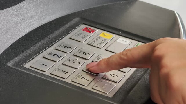Close-up view of a finger pressing numeric buttons on an ATM keypad, entering a personal identification number with Cyrillic and English labels on dark gray banking machine in a financial transaction