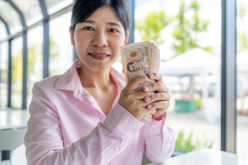 Confident Asian woman holding Thai baht banknotes, Money, Cash, Wealth, symbolizing financial stability, income growth, and personal success