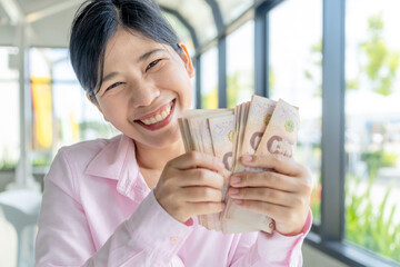 Money, Cash, Wealth, Happy Asian woman holding Thai baht banknotes, showing wealth, success, and financial happiness, close-up
