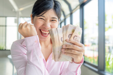 Money, Cash, Wealth, Excited Asian woman holding Thai baht banknotes and celebrating financial success with a bright smile and winning gesture