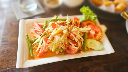Papaya Salad Delight: A vibrant plate of Papaya salad, bursting with fresh vegetables and enticing flavors, presented on a square plate and ready to eat. 