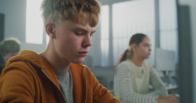 Close Up of Male Student in Orange Hoodie Works on Computer Writing Code for Game Development Project. Young Man Studies Modern Programming. Future IT Careers, Education, and Creativity. Portrait.