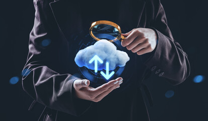 Business person holding magnifying glass over holographic cloud with data arrows, symbolizing online storage and internet network analysis concept.