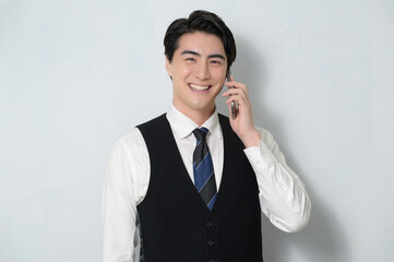 スマホで通話をするベストを着た日本人男性
