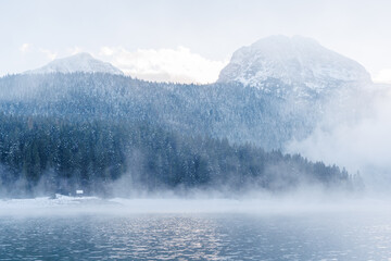 Lake in Montenegro at sunset with mist over the water and snowy mountain peaks