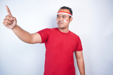Naklejka premium A young Asian man with a happy successful expression, raised a fist wearing red shirt and flag headband isolated by white background. Indonesia's independence day concept.