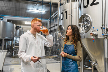 Brewery workers performing quality control, tasting beer sample from production tank. Industry professionals ensuring craft beer standards