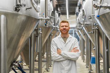 Happy male brewer or lab technician standing with arms crossed in a microbrewery production facility looking at camera